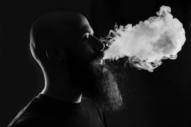 A man with a beard exhaling a cloud of smoke