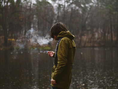 A man in a hoodie smoking in front of a lake