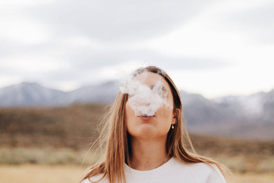 Woman smoking 2 hitter pipe outside with mountains in the distance